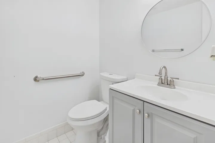 Bathroom featuring a vanity with a light gray cabinet, white countertop, integrated sink, and a circular mirror