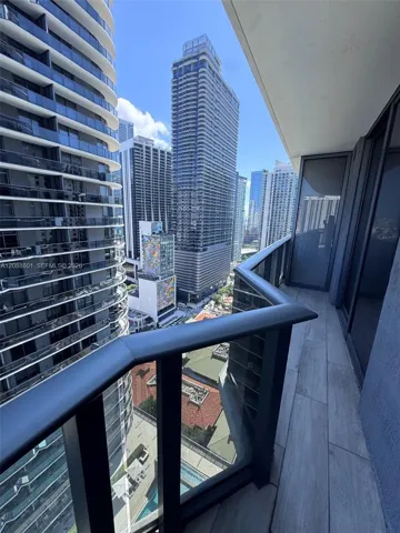 Private balcony featuring wood-finish tile flooring, glass panel railing with a dark metal handrail, and high-rise cityscape surroundings