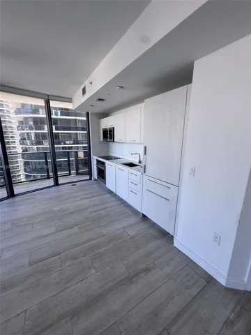 Modern kitchen featuring light wood-finish cabinetry, floor-to-ceiling windows, integrated panel-ready appliances, and wood-finish flooring