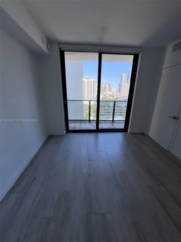 Wood-finish flooring, sliding glass balcony door, metal balcony railing, and high-rise urban skyline scenery