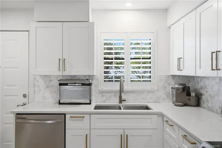 Quartz countertops, white shaker-style cabinetry, modern hardware, and a double-basin sink create a clean, coastal-inspired look.