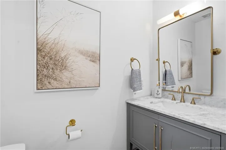Coastal-inspired bathroom pairs a marble-look vanity with warm brass-tone fixtures and a streamlined, updated design.