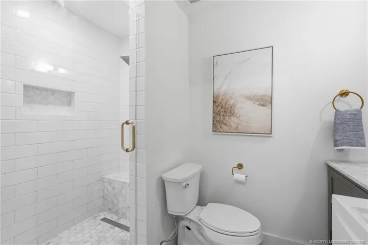 Updated walk-in shower features crisp subway tile, a decorative tile floor, built-in niche, bench, and glass enclosure.