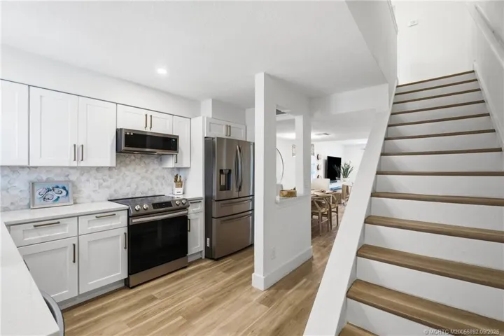 Updated kitchen features crisp white cabinetry, quartz countertops, stainless steel appliances, a decorative tile backsplash, and warm wood-look flooring.