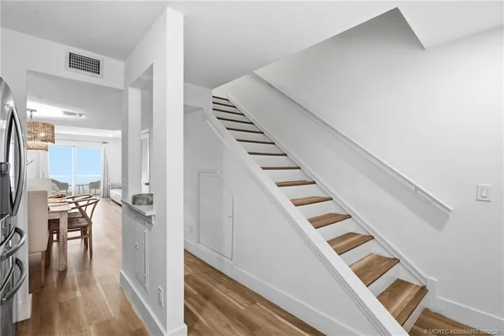 The kitchen flows toward the dining and living areas, while the staircase provides access to the upper level.