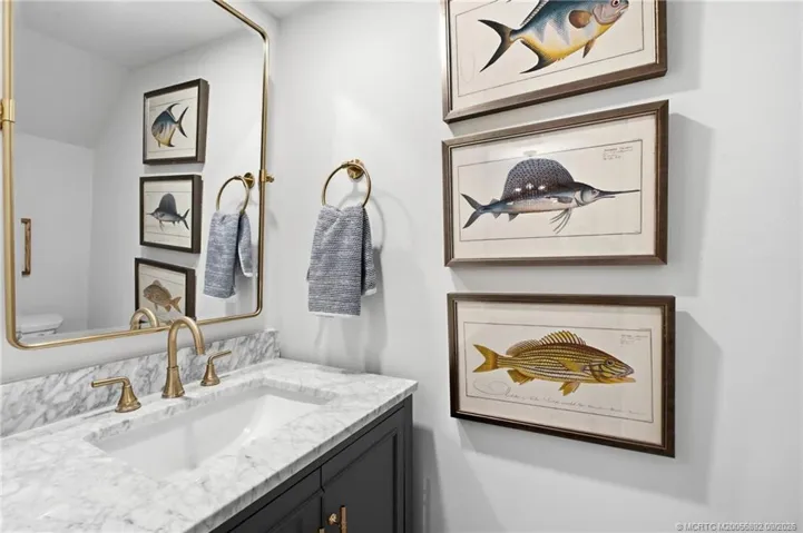 Updated half-bathroom features a marble-look vanity top, dark cabinetry, brass-tone fixtures, and a coordinating framed mirror.