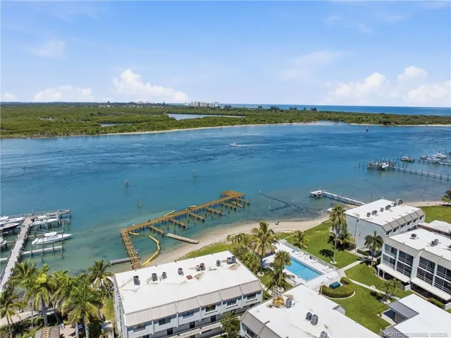 Aerial view showcases the community pool, waterfront grounds, sandy shoreline, and dock area.