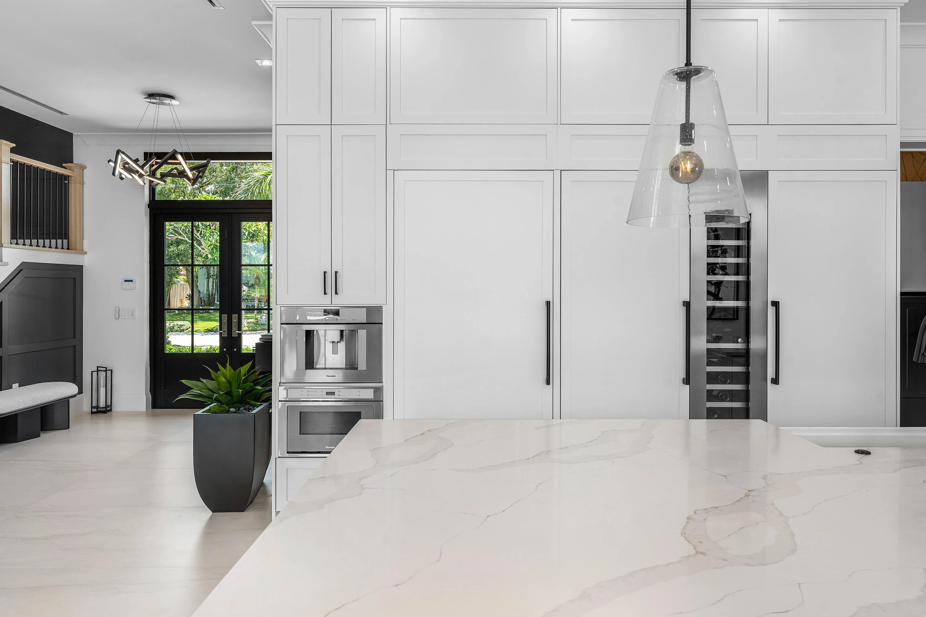 Integrated paneled refrigerators, built-in coffee system, wine refrigerator, expansive island with light-toned countertop, and double glass-paneled entry doors
