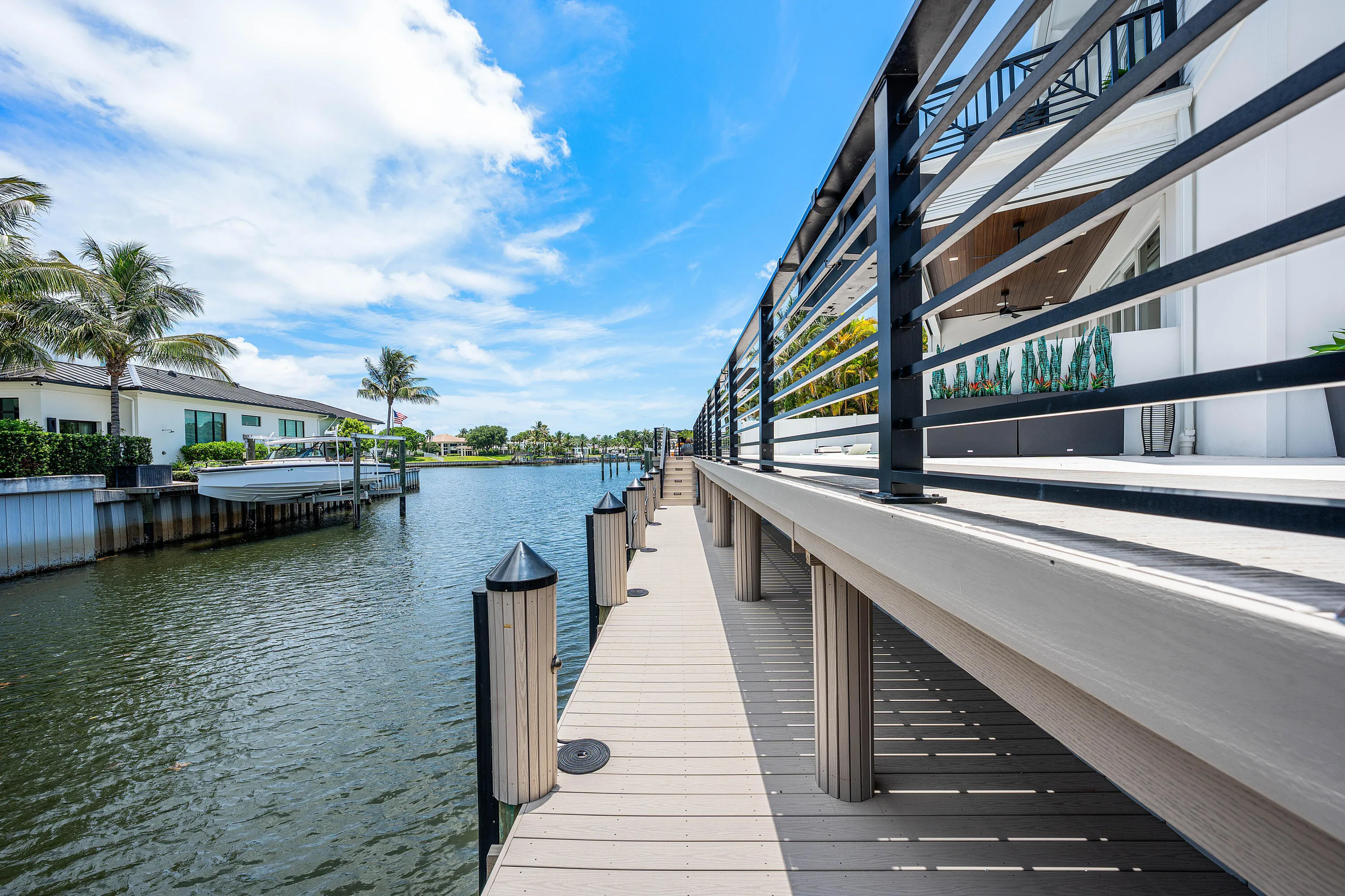 Waterfront property featuring a private dock with pilings, a boat lift, and a spacious deck with contemporary metal railings