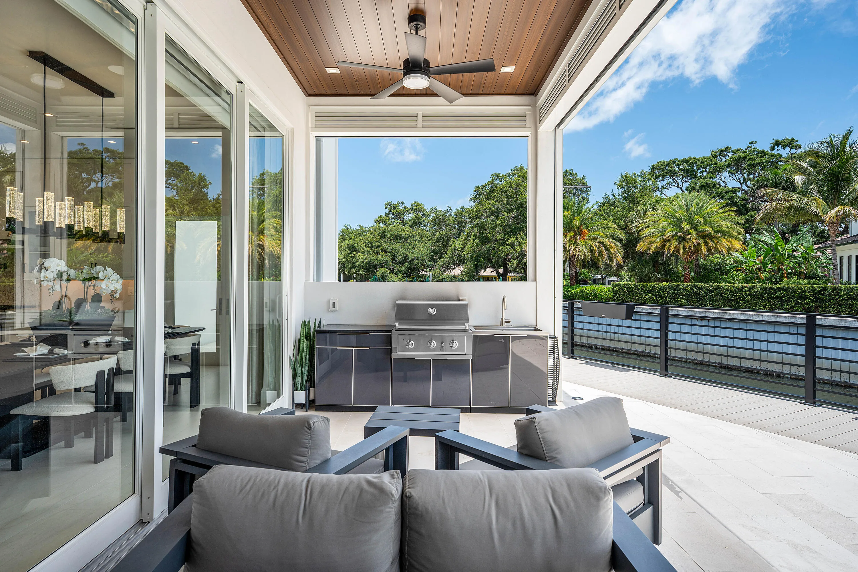 Expansive outdoor living area with wood-finish ceiling, built-in outdoor kitchen with grill and sink, ceiling fan, and large sliding glass doors