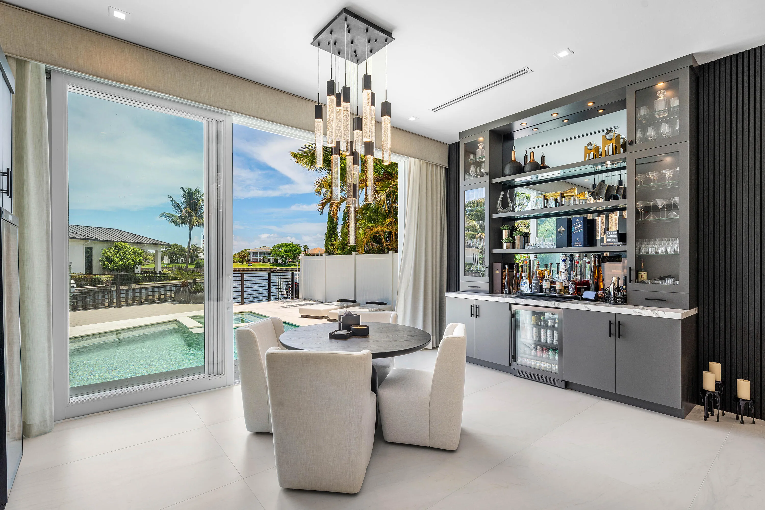 Floor-to-ceiling sliding glass doors, built-in wet bar with mirrored backsplash, integrated beverage refrigerator, modern pendant lighting, and light-toned tile flooring
