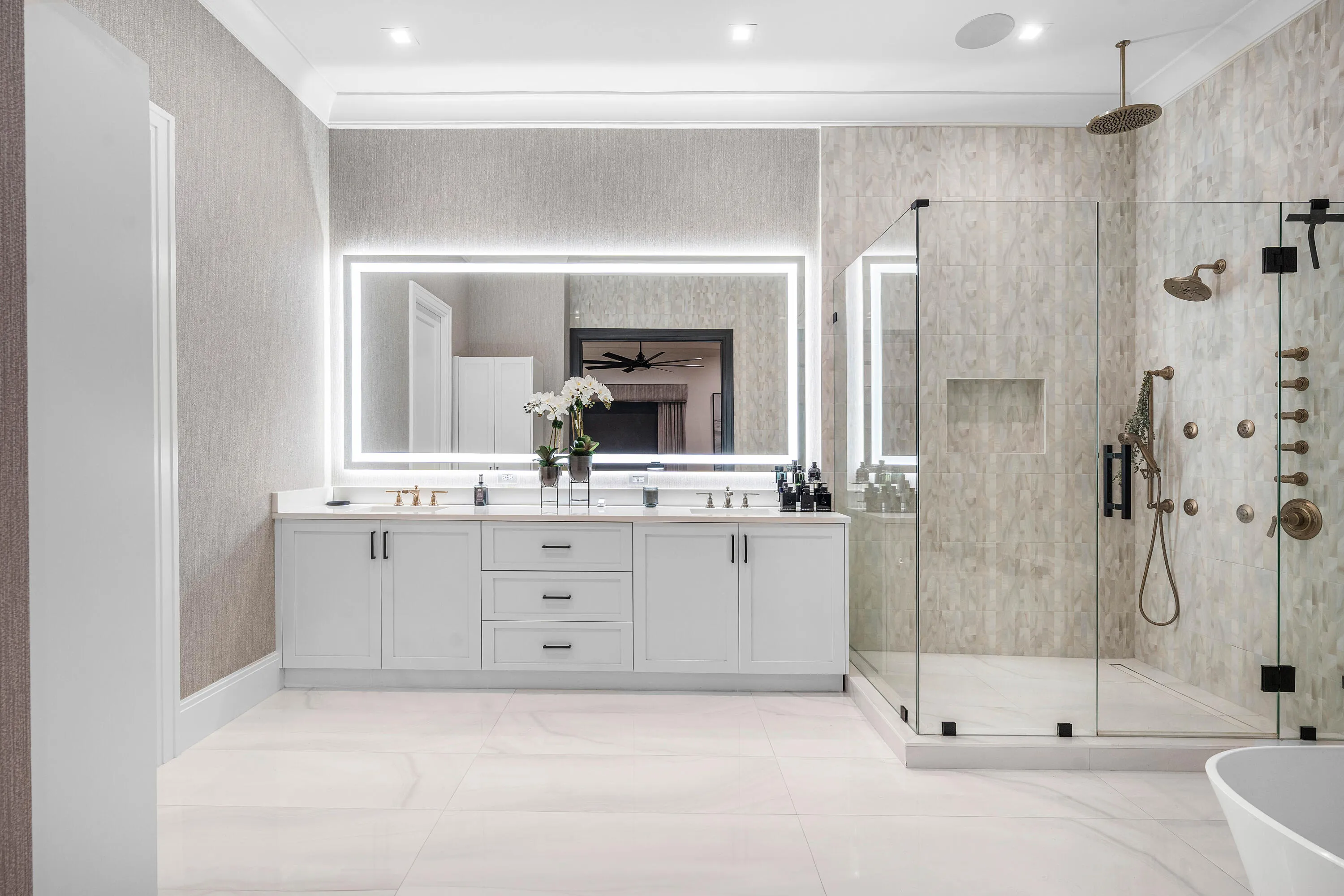 Spa-inspired primary bathroom featuring a dual-sink vanity with white cabinetry, polished quartz countertops, and integrated undermount sinks + large glass shower enclosure and modern mirror