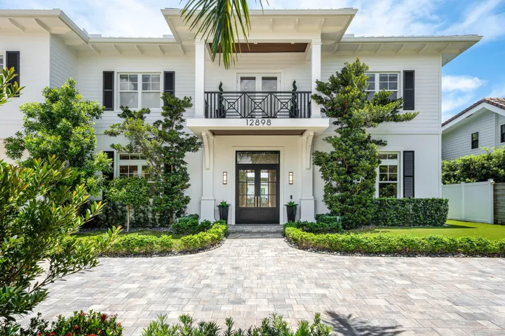 White exterior with black shutters, double-door entry, a second-story balcony with an iron railing with mature landscaping.