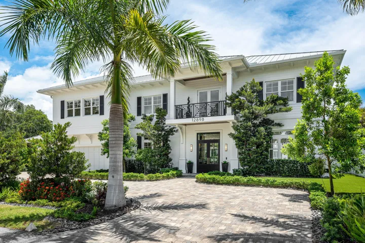 Two-story white exterior with dark shutters, metal roof, and an oversized paved circular driveway