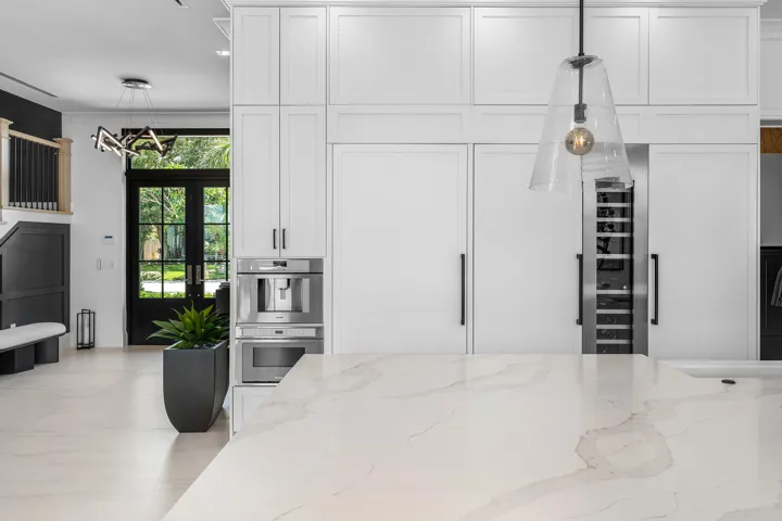 Integrated paneled refrigerators, built-in coffee system, wine refrigerator, expansive island with light-toned countertop, and double glass-paneled entry doors