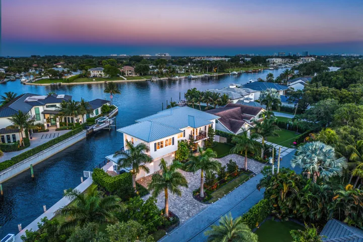 Waterfront property featuring a private boat dock, mature palm trees, paved driveway, and lush landscaping