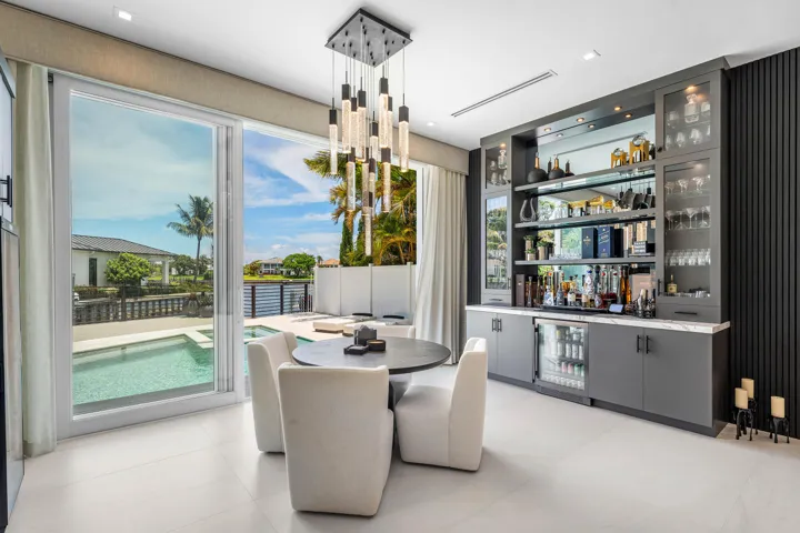 Floor-to-ceiling sliding glass doors, built-in wet bar with mirrored backsplash, integrated beverage refrigerator, modern pendant lighting, and light-toned tile flooring