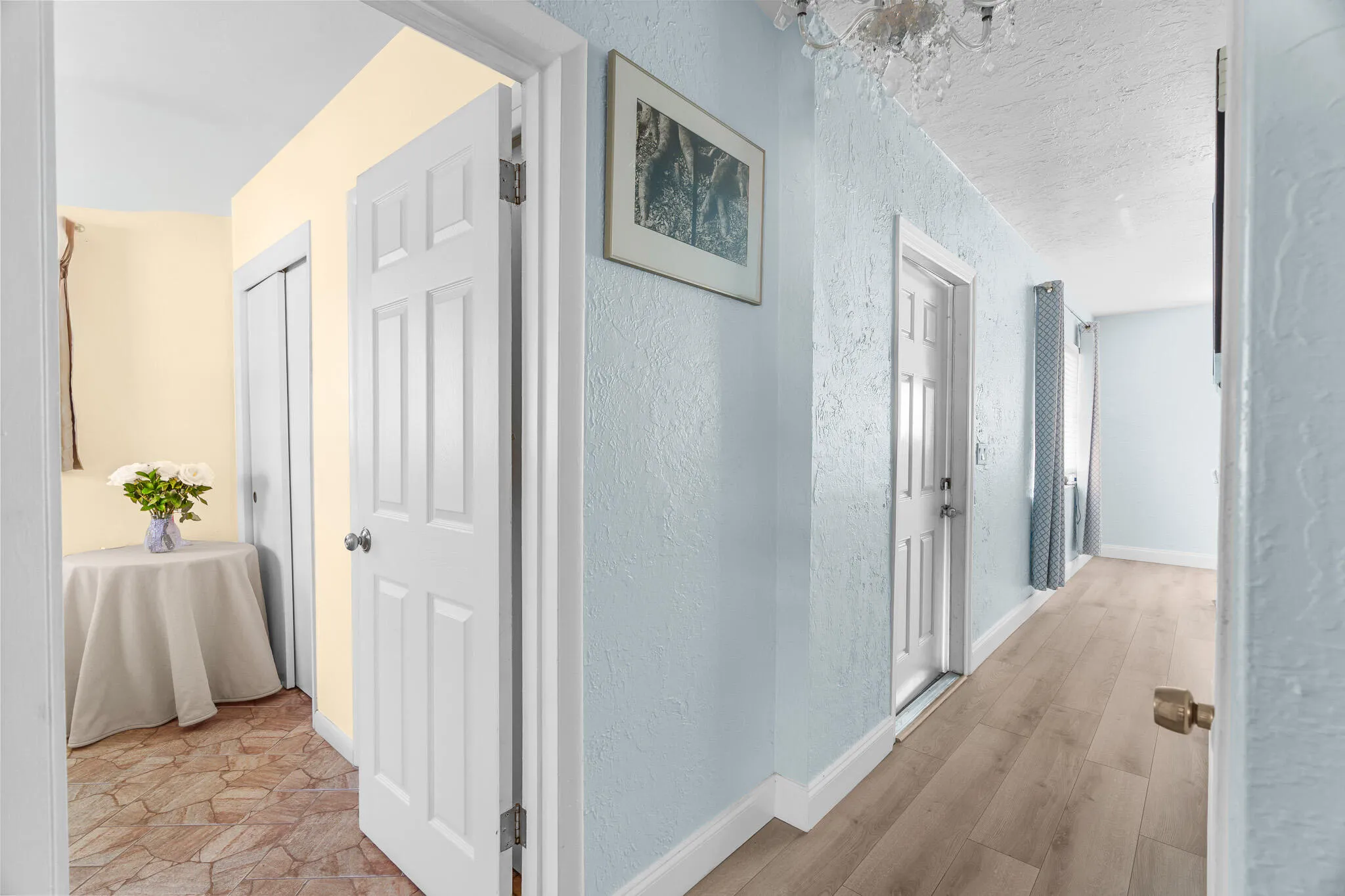 Hallway featuring wood-finish flooring, light blue wall texture, and white paneled doors