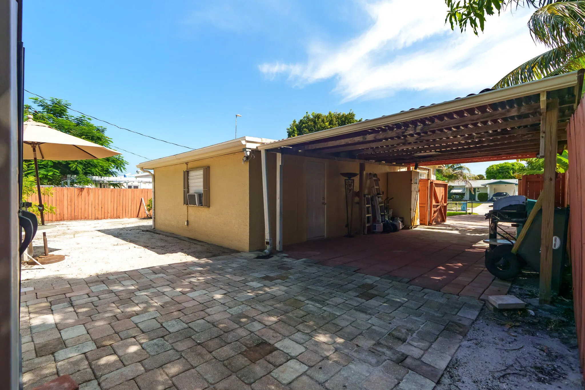 Paver backyard, covered carport structure, wood fencing, and an exterior storage area
