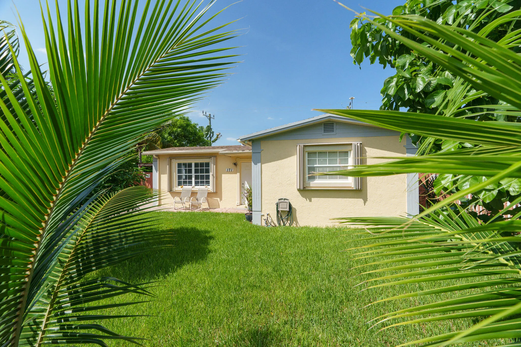 Exterior featuring a stucco finish, gabled roofline, front lawn, and prominent palm foliage