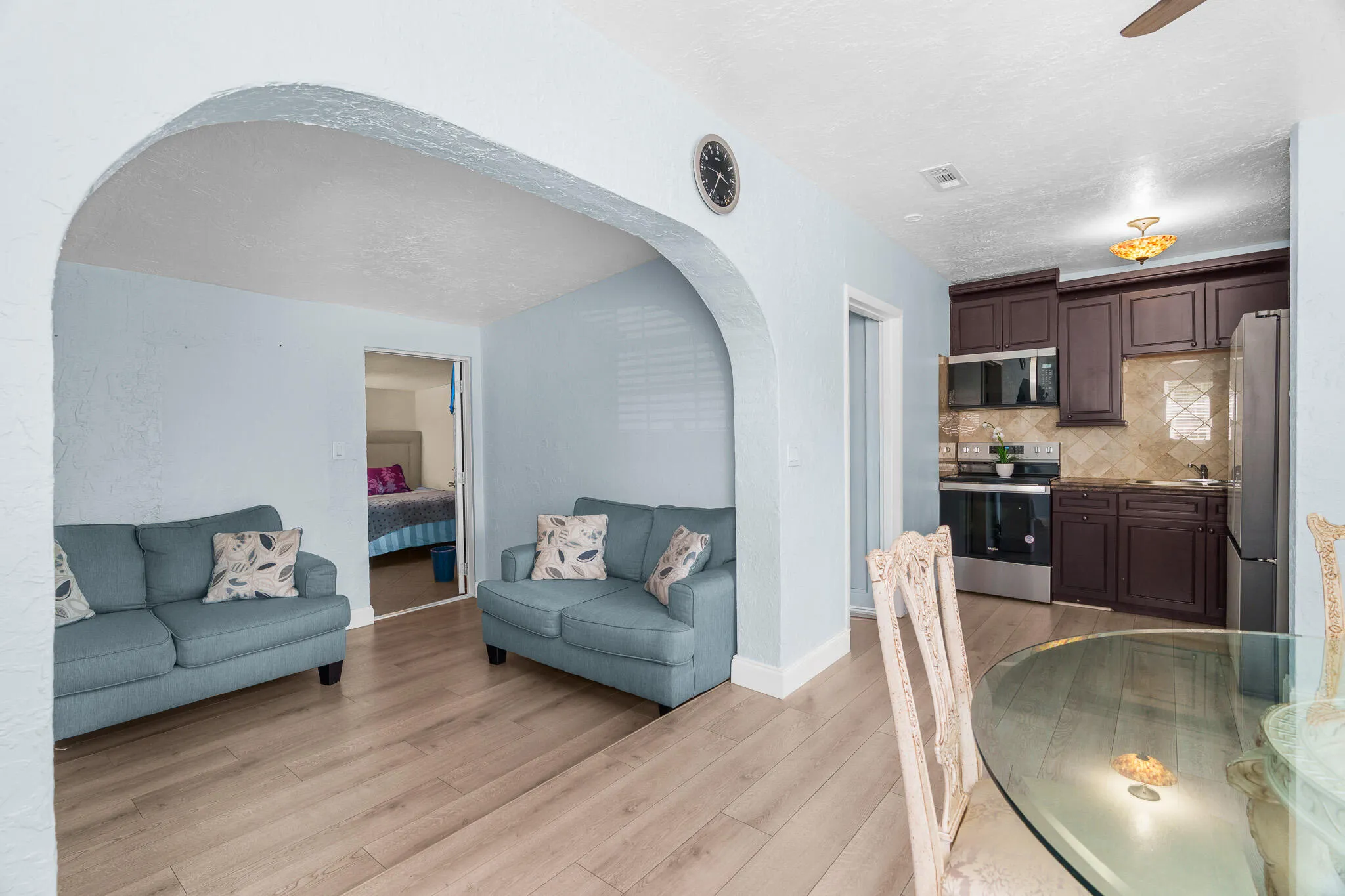 Wood-finish flooring throughout, arched entryway, updated kitchen with stainless steel appliances, dark wood cabinetry, and a patterned backsplash
