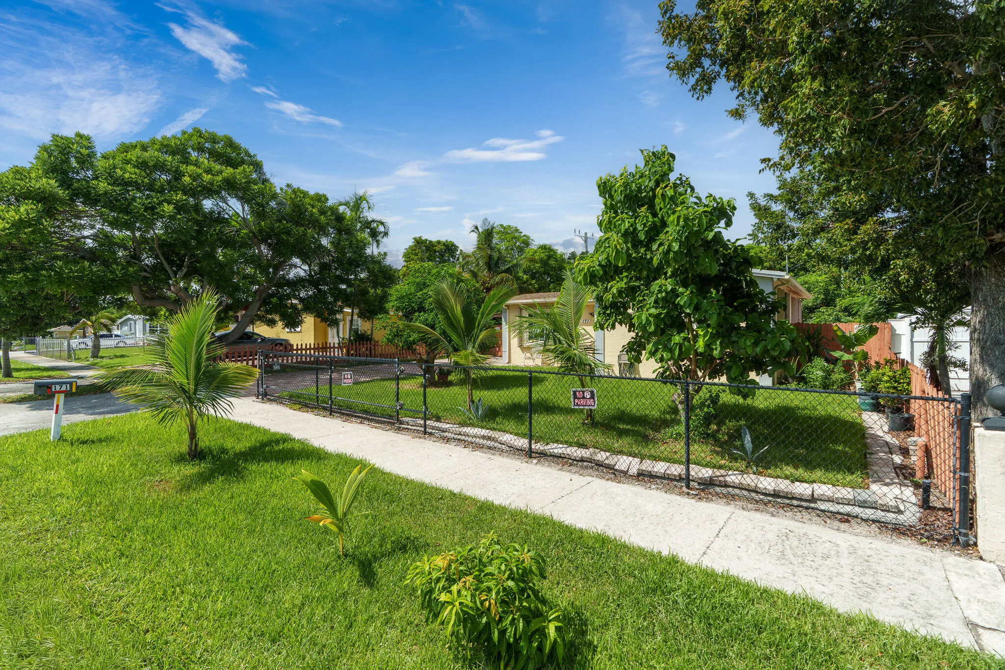 Fenced front yard with mature trees and a concrete walkway