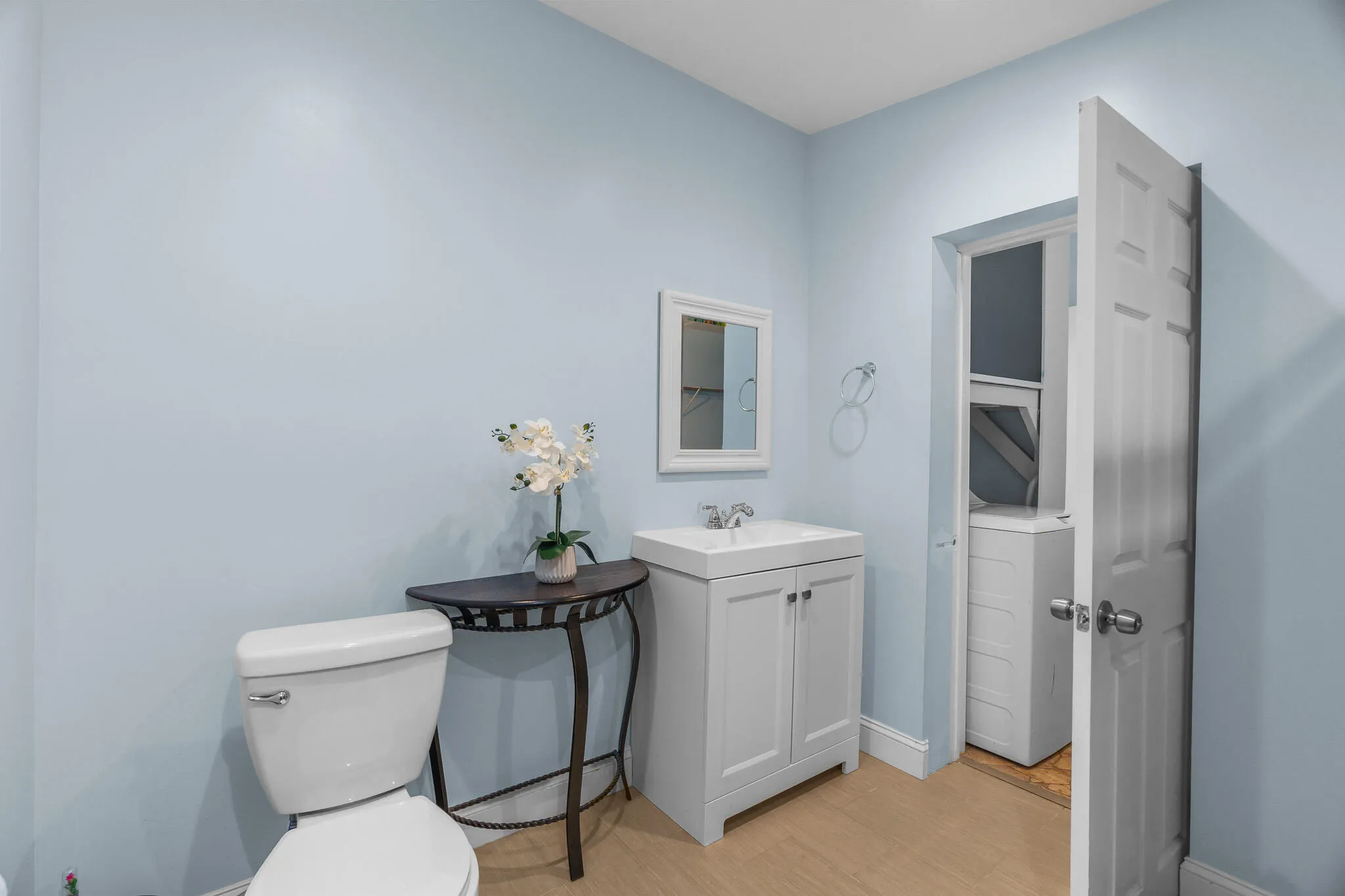 Light blue wall finish in this bathroom featuring a white vanity with integrated sink, white framed mirror, and wood-finish flooring