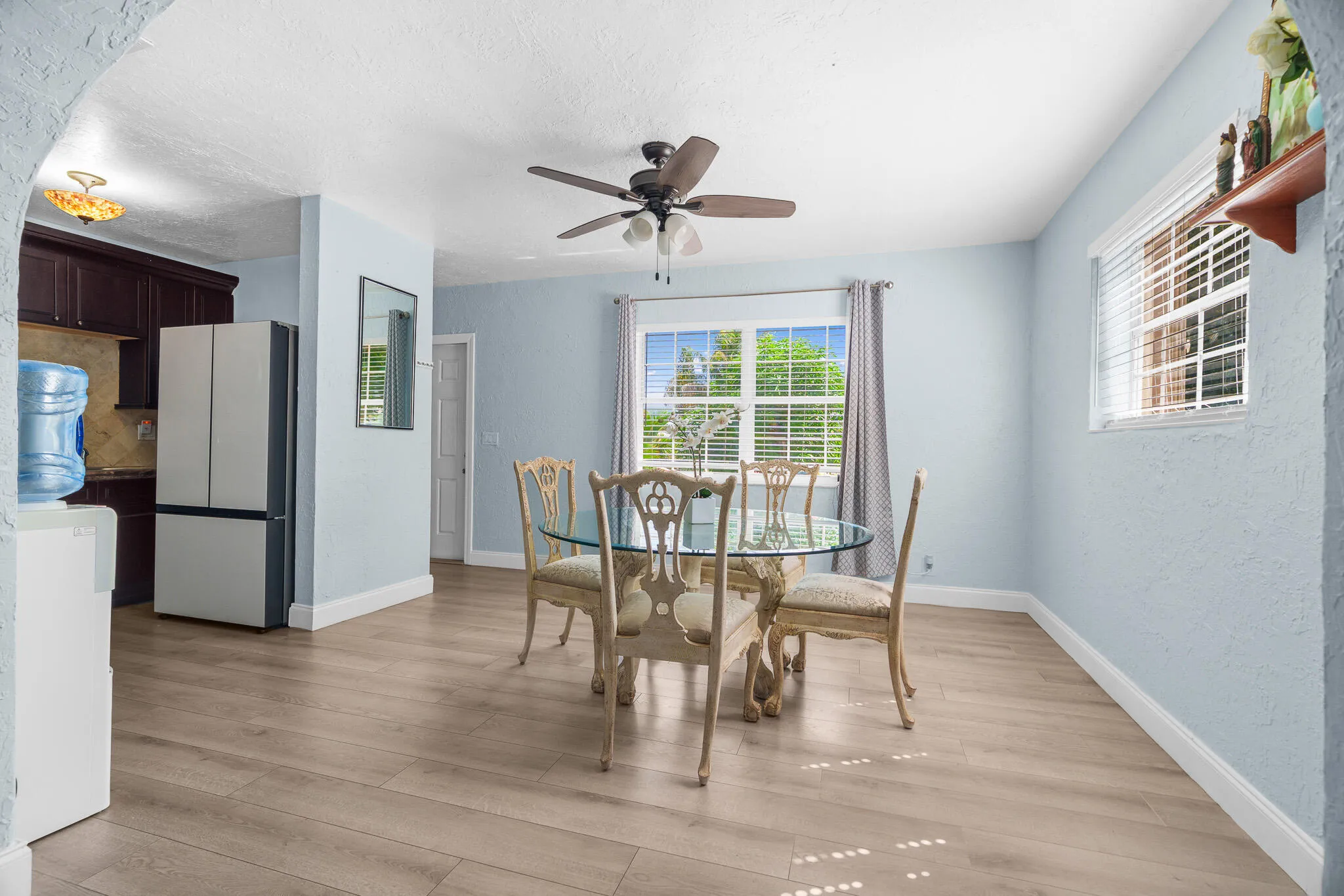 Wood-finish flooring throughout, light blue wall paint, multiple windows, and ceiling fan with integrated lighting