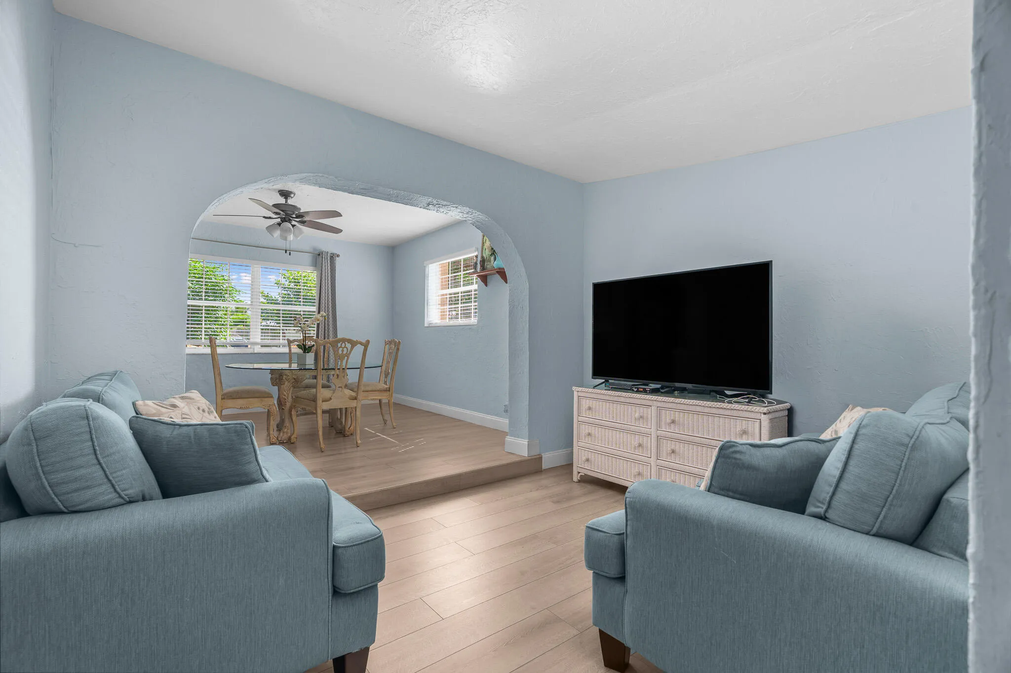 Archway entry, light blue wall paint, wood-finish flooring, ceiling fan, natural light windows