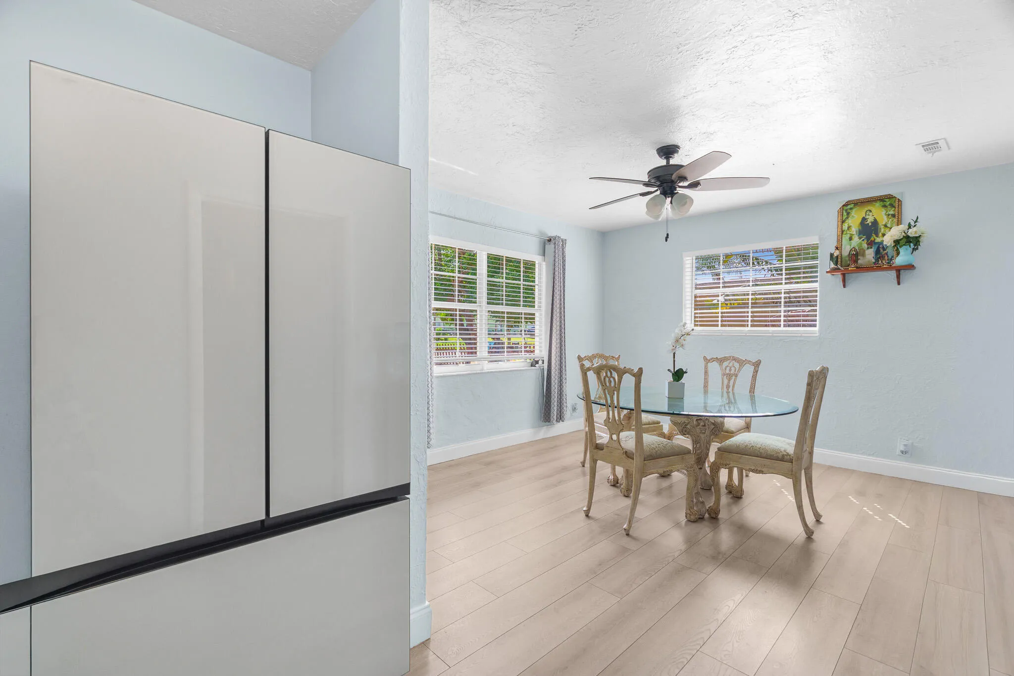 Light-toned wood-finish flooring, two large windows, and a ceiling fan with integrated lighting