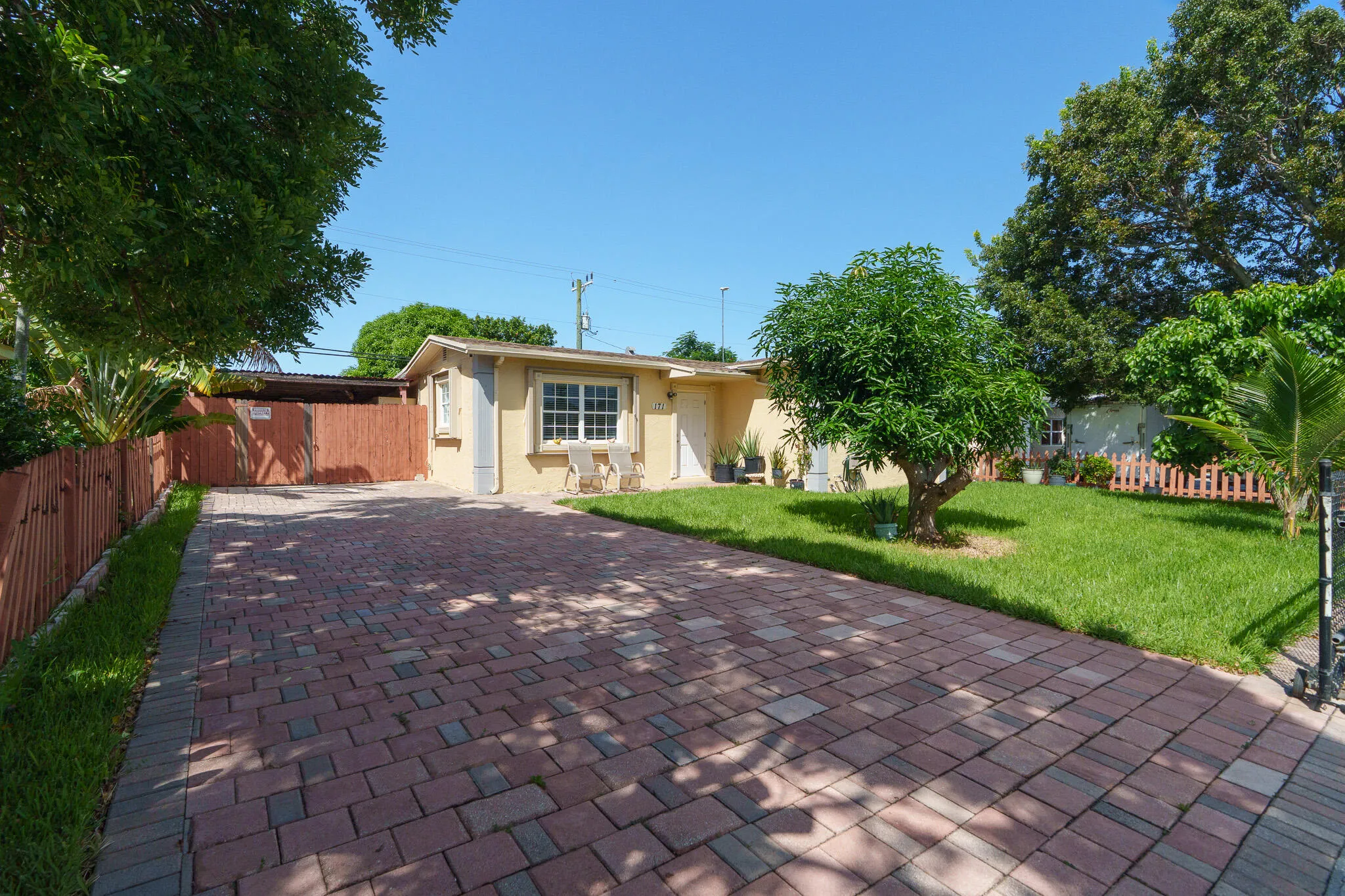 Paved brick driveway leading to a covered carport, stucco exterior, and a manicured lawn
