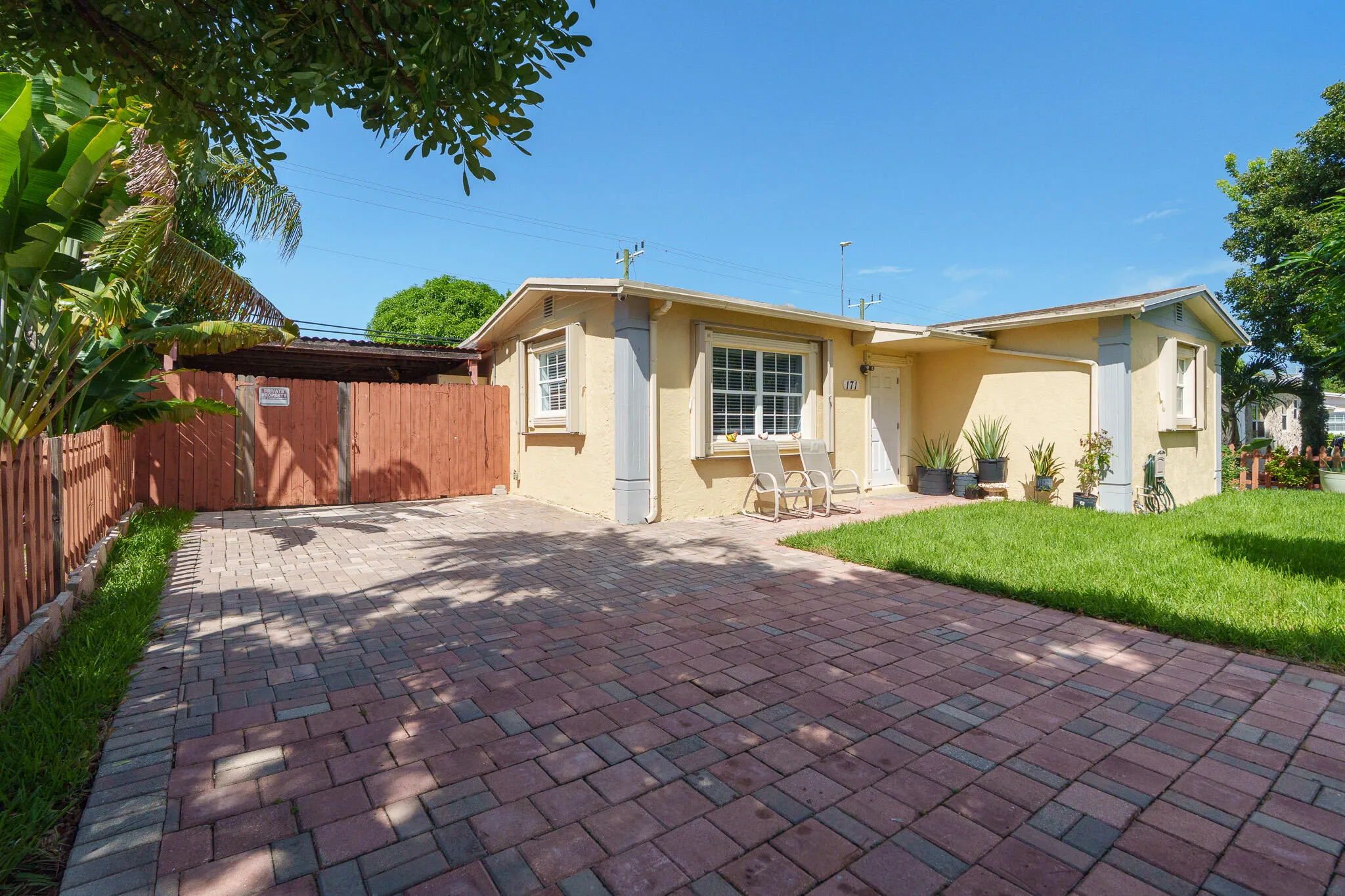 Paved driveway with brick pavers, stucco exterior, fenced yard, and a covered entry