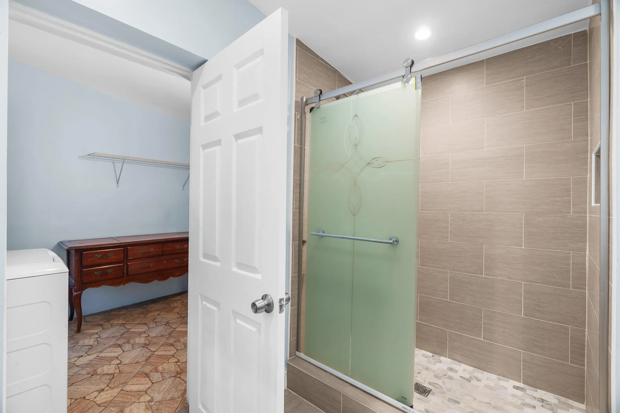 Frosted glass sliding shower door with decorative etching, large format wall tiles, and mosaic tile shower pan