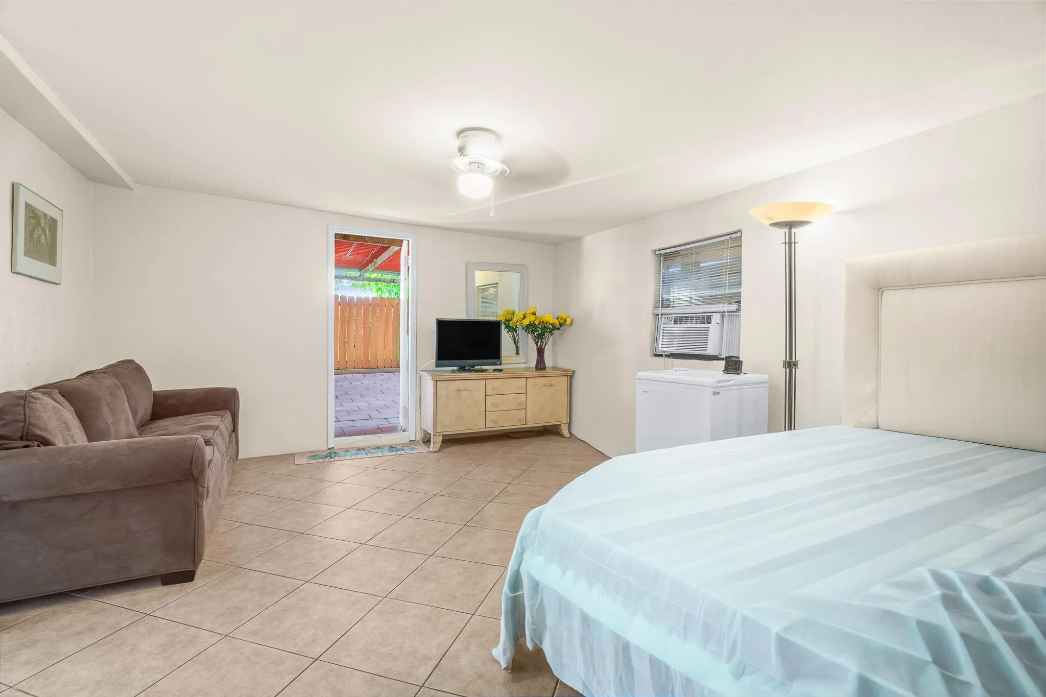 Ceramic tile flooring, white walls, ceiling fan, window with horizontal blinds, and an exterior door providing direct outdoor access