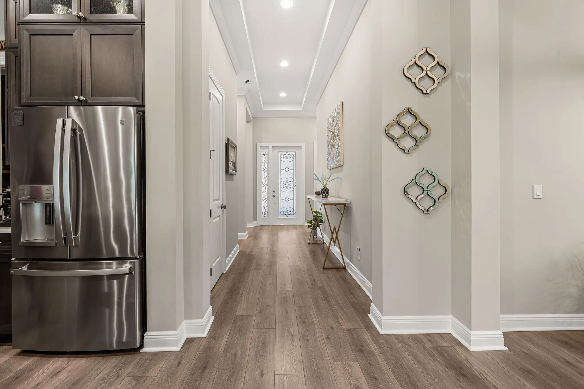 Recessed lighting illuminates the hallway, featuring crown molding and wide plank wood-look tile flooring
