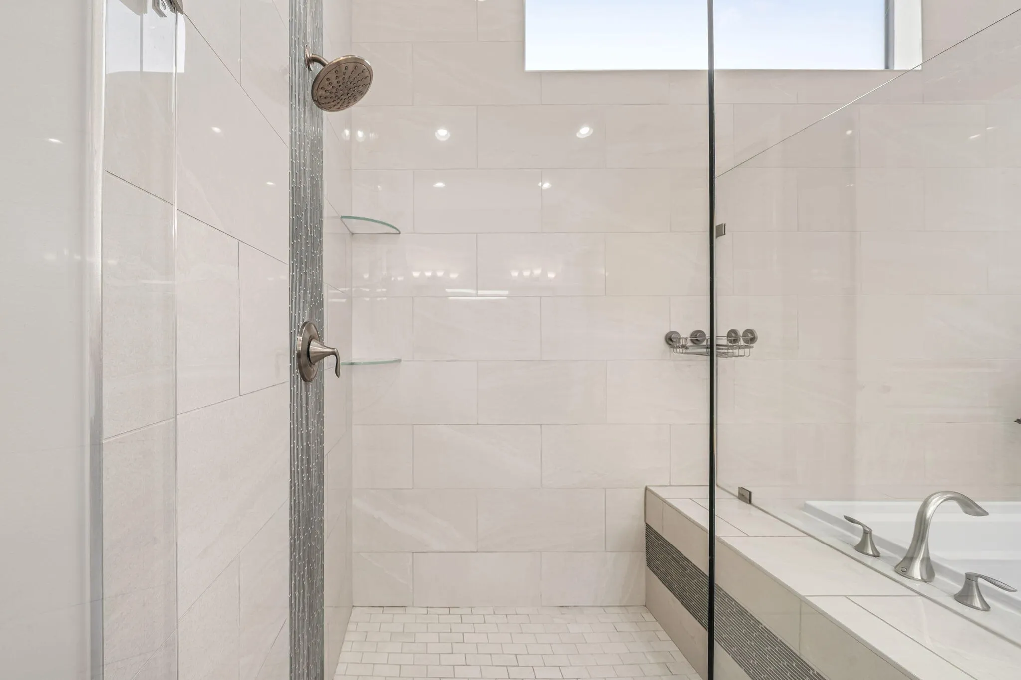 Shower with a glass enclosure, white rectangular wall tiles, mosaic tile shower floor, and a built-in shower bench