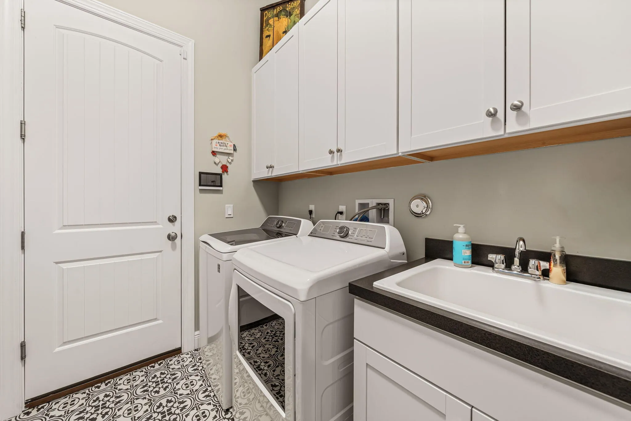 Laundry area featuring a utility sink, white cabinetry with brushed nickel hardware, and patterned floor tiling