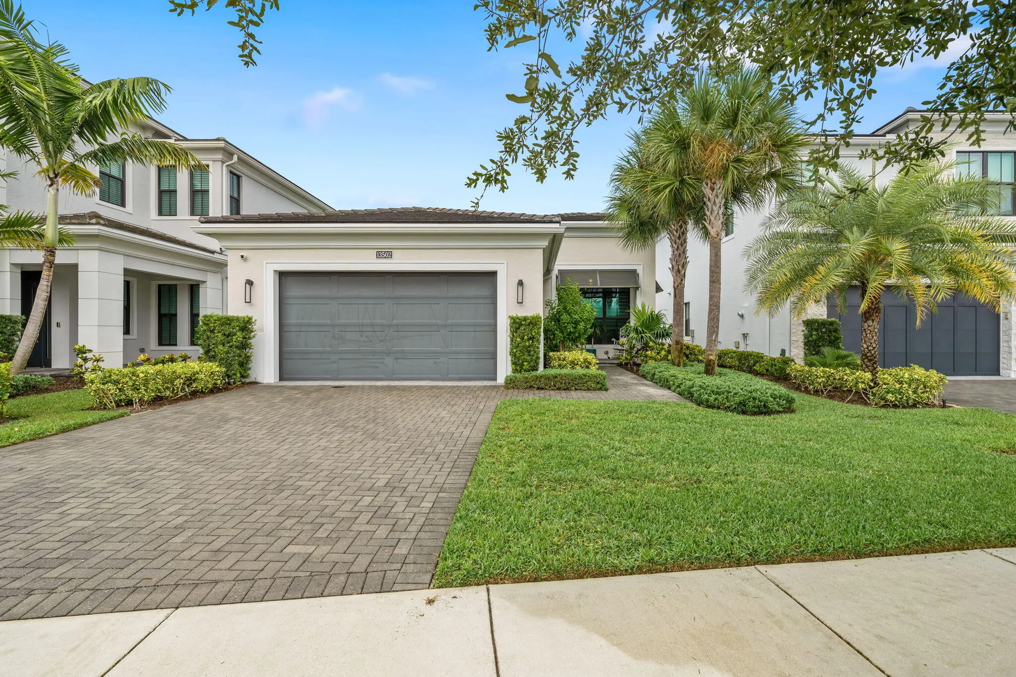 Contemporary architecture with a two-car garage, paver driveway, and established landscaping