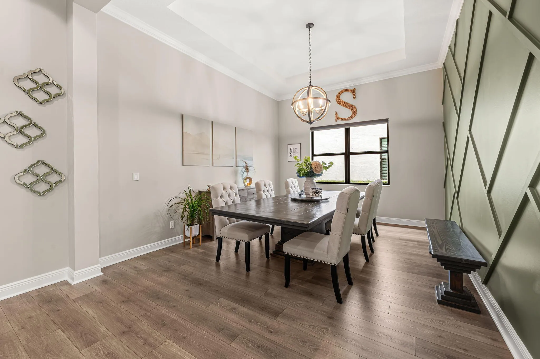 Tray ceiling with recessed lighting, accent wall with geometric paneling, large window, and suspended spherical chandelier