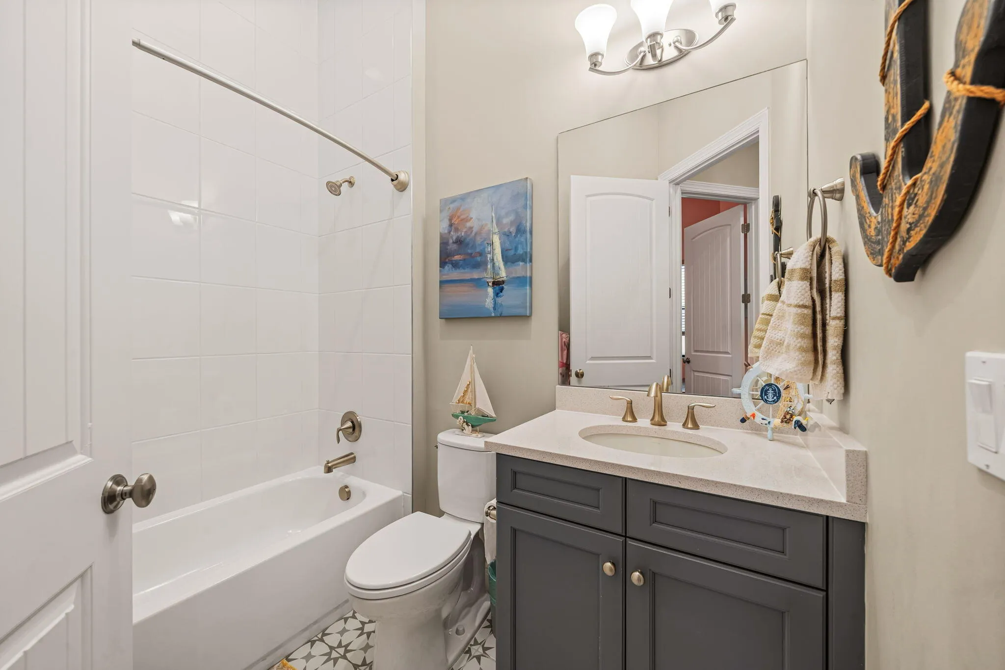 White subway tile shower surround with a built-in tub, patterned floor tile, single vanity with a gray cabinet, and a wall-mounted mirror
