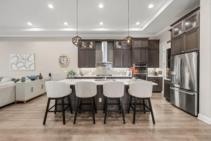 Kitchen featuring an oversized island, stainless steel appliances, dark wood cabinetry, under cabinet lighting, recessed lighting, and wide plank wood-look tile flooring
