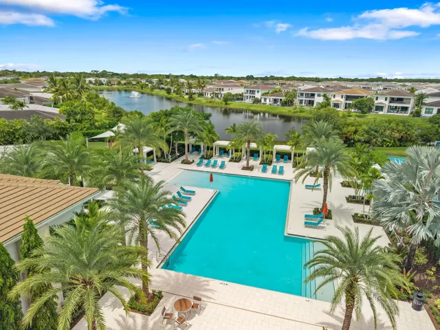 Community pool with surrounding lounge areas, mature palm trees, and a lake with a fountain