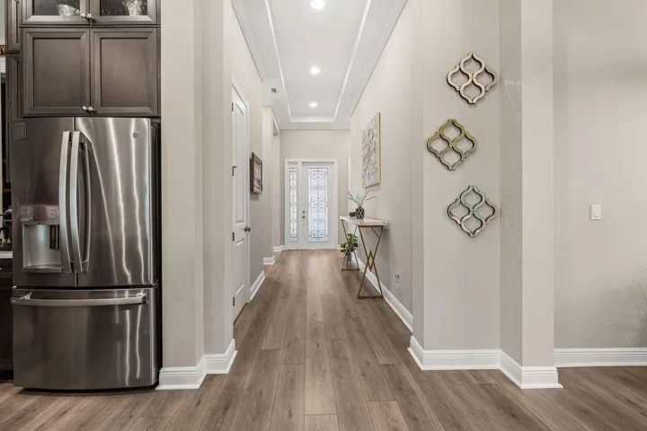Recessed lighting illuminates the hallway, featuring crown molding and wide plank wood-look tile flooring
