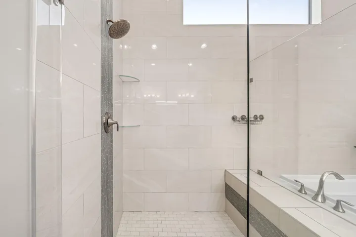 Shower with a glass enclosure, white rectangular wall tiles, mosaic tile shower floor, and a built-in shower bench