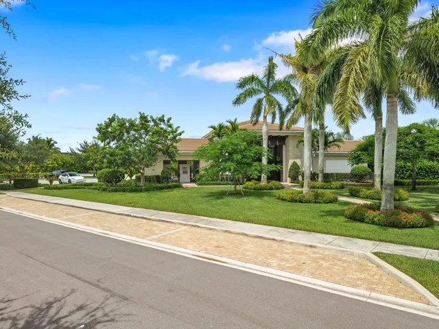 Lush landscaping with mature palm trees, expansive green lawn, paver-style sidewalk, and a multi-story entrance