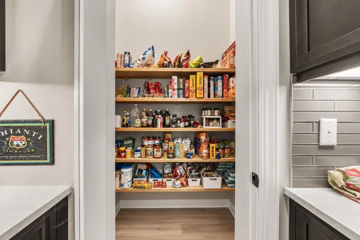 Pantry with multiple wood shelves, light grey subway tile backsplash, and light-toned Quartz countertops