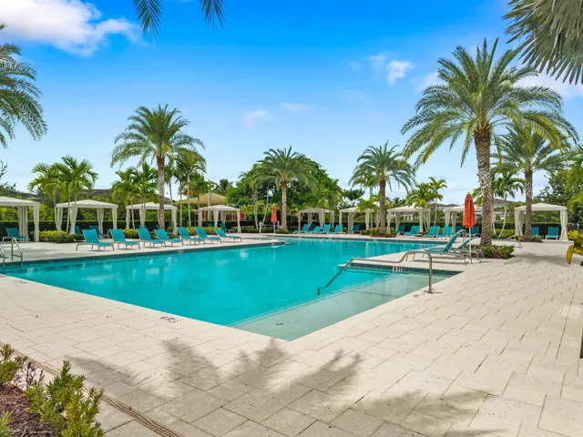 Expansive outdoor pool with integrated steps, surrounded by extensive paver decking, multiple private cabanas, and mature palm trees