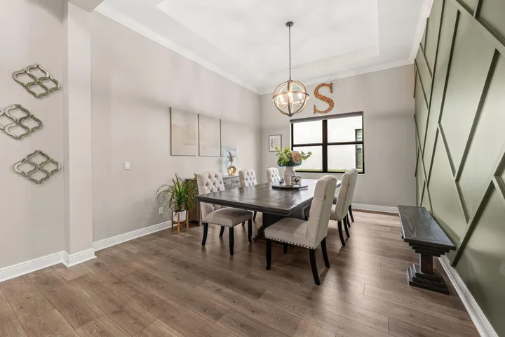 Tray ceiling with recessed lighting, accent wall with geometric paneling, large window, and suspended spherical chandelier