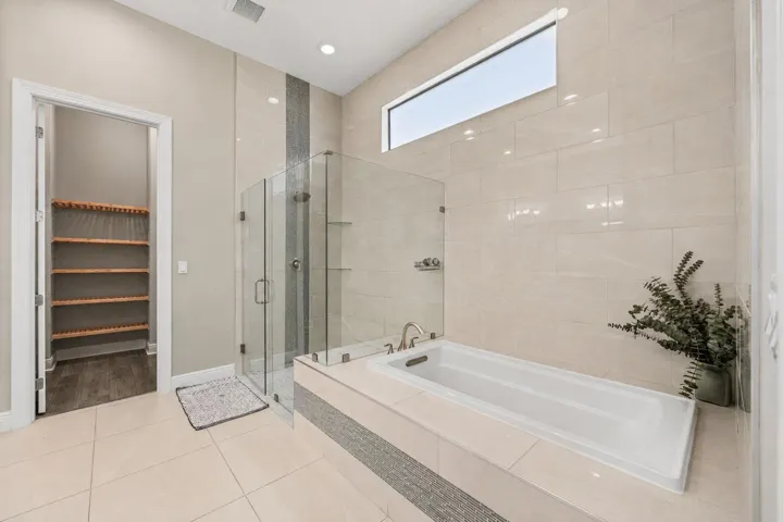 Soaking tub with brushed nickel fixtures, glass-enclosed shower and light-toned wall tiling.