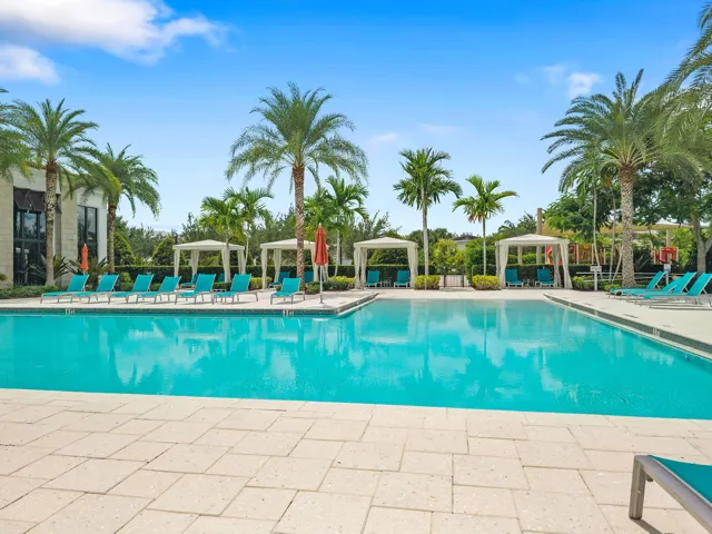 Expansive outdoor swimming pool with surrounding paver decking, multiple sun loungers, and shaded cabanas